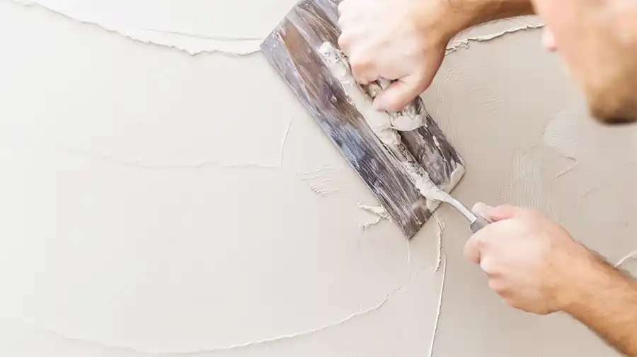 stukadoor die een muur glad pleistert met een troffel